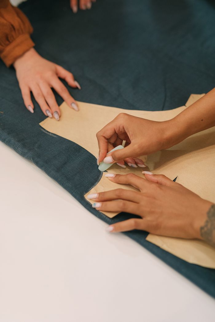 About Close-up of hands marking a garment pattern, showcasing the craft of tailoring.