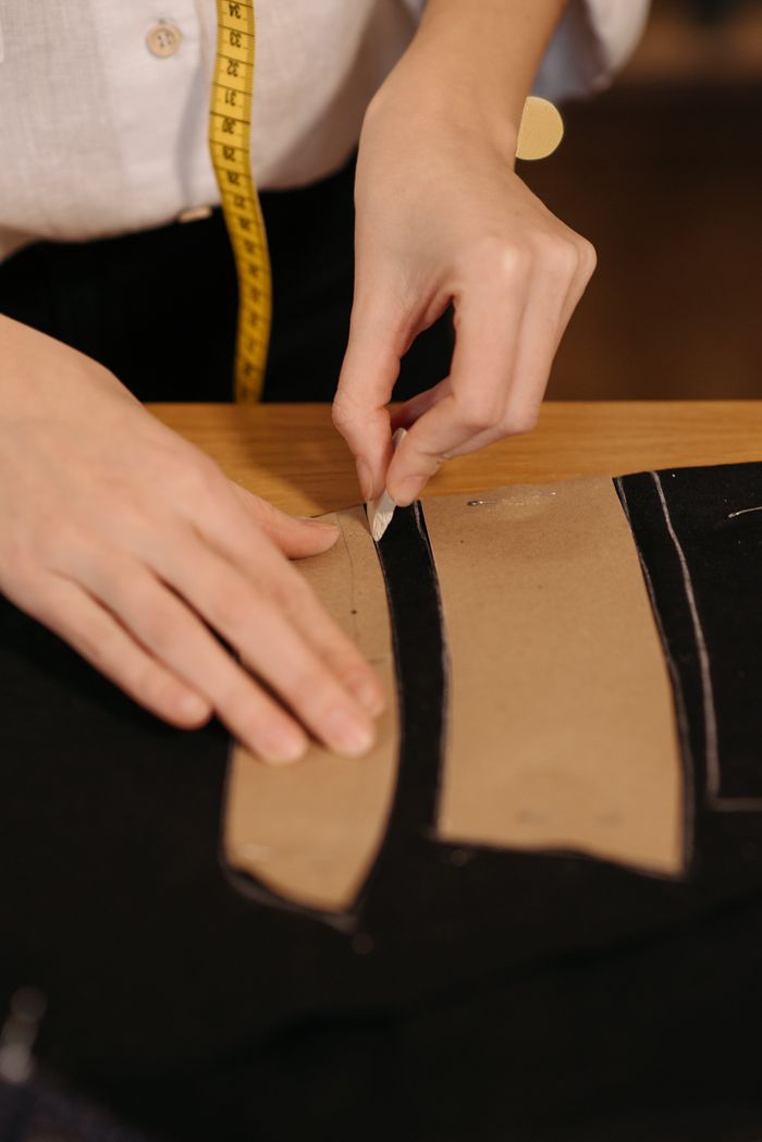 Close-up of a tailors hands tracing a sewing pattern on black fabric with precision and skill.